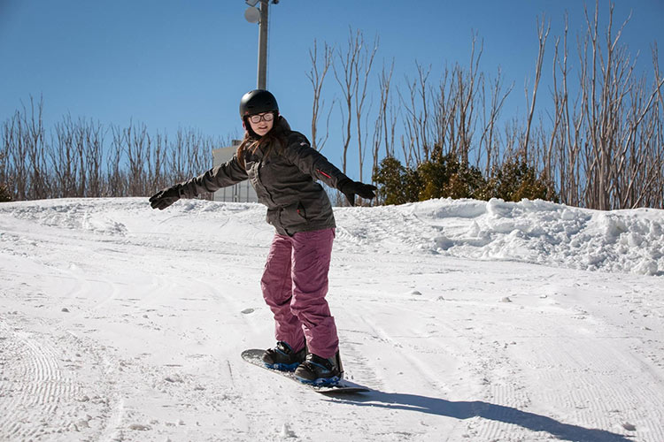 a girl in winter snow clothes riding down the hill on a snowboard