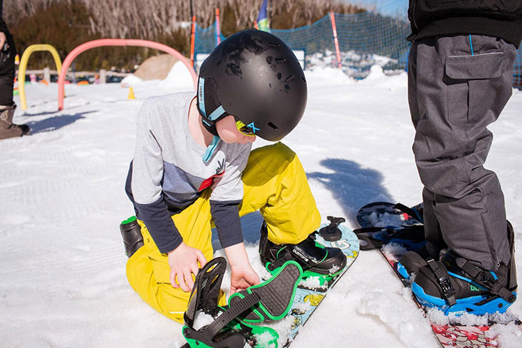 a kid sitting on the snow with a snowboard helmet on