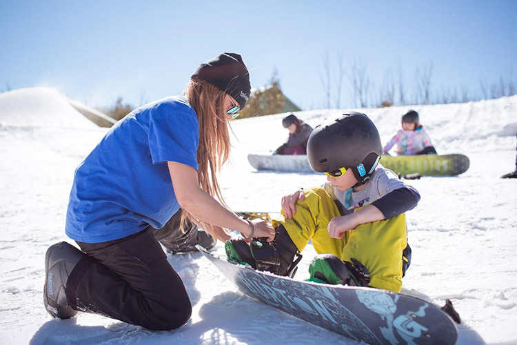 a ski instructor helping to strap a kid into their snowboard
